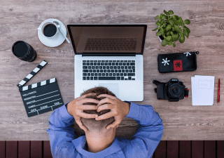 A man sitting in front of the computer and holding his head.