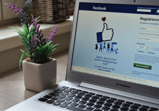 A vase with purple flowers and a laptop showing the registration page of Facebook.
