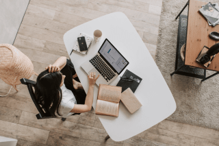 A woman working on her laptop surrounded by books and notebooks.