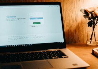 A laptop showing the login page of Facebook and a vase of flowers.